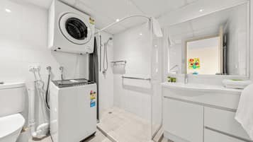 A modern bathroom with a built-in washing machine, a shower with a glass door, and a sink with a mirror.