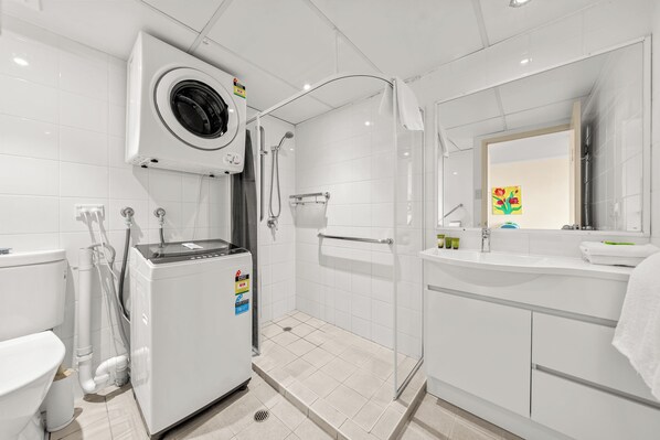Un baño moderno con lavadora integrada, ducha con puerta de cristal y lavamanos con espejo.