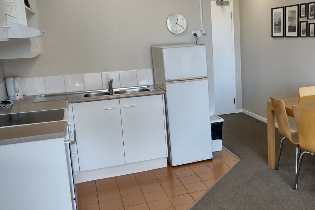 A compact kitchen with white cabinets, a sink, and a refrigerator. There is a dining area with a table and chairs.