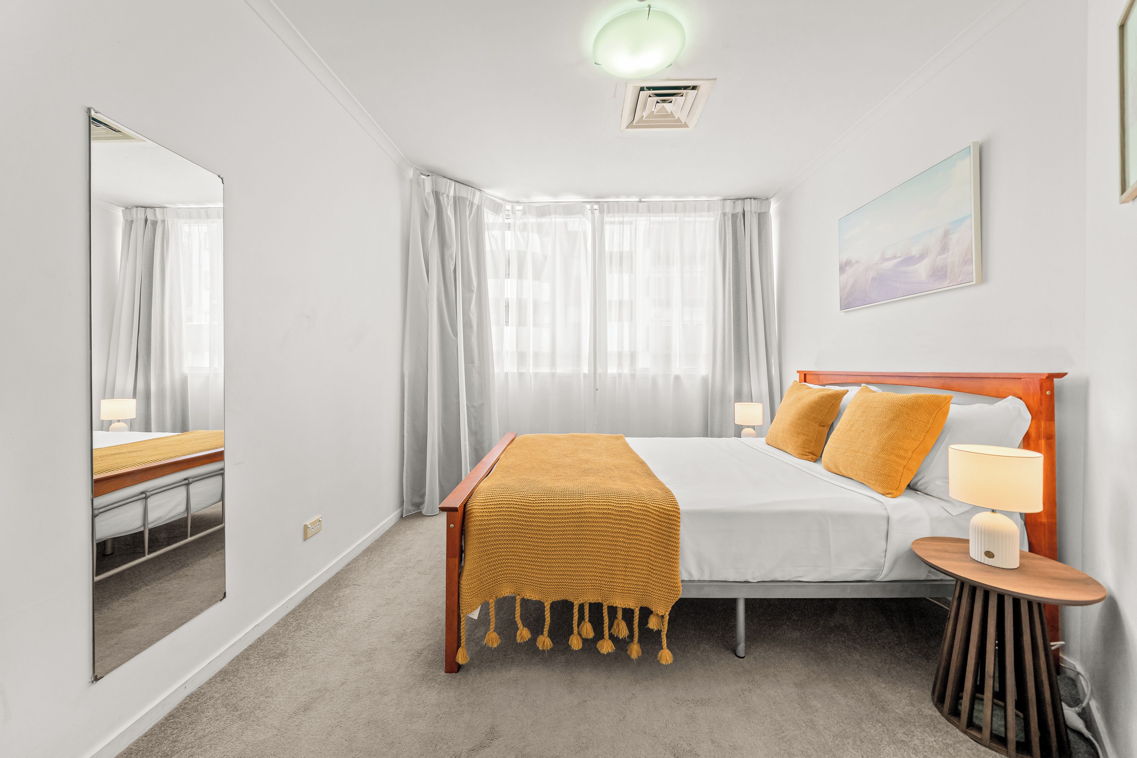 Una habitación de hotel con cama, mesita de noche, lámpara y un cuadro en la pared.