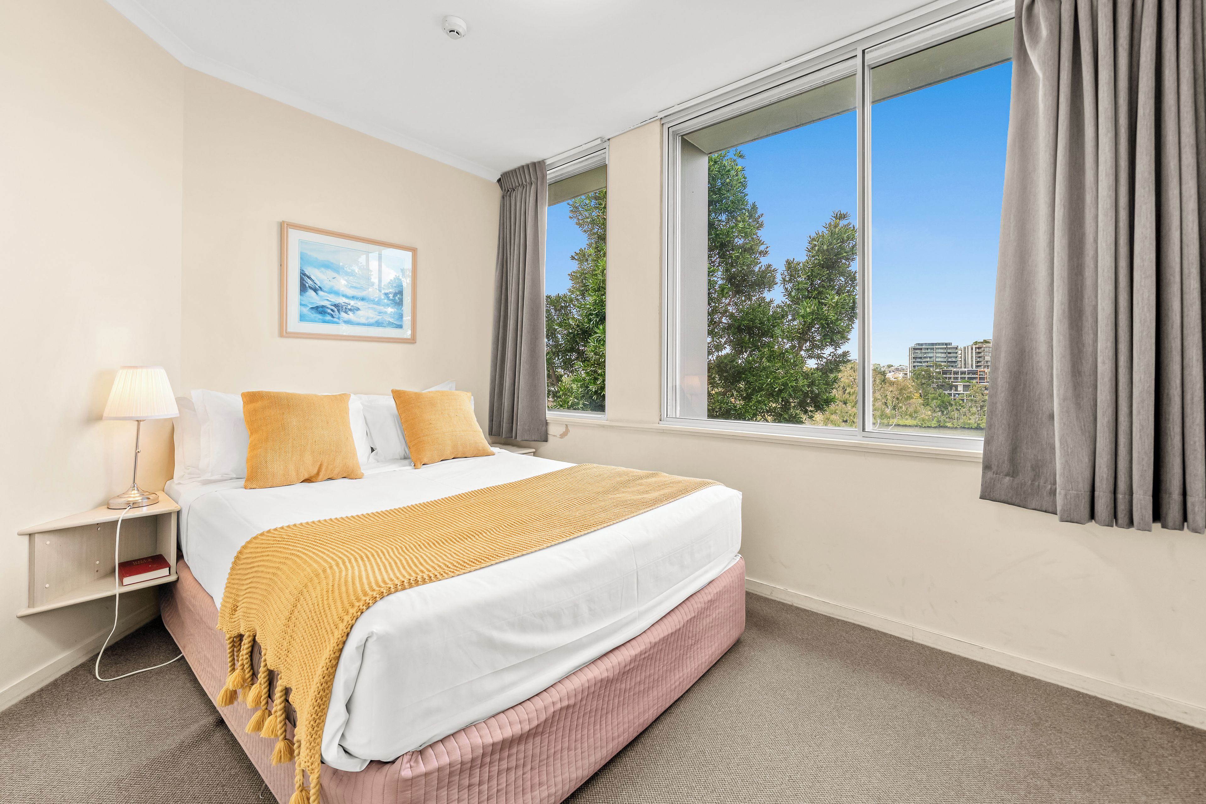 Una habitación de hotel con una cama, una mesita de noche, una lámpara, un cuadro y una ventana con cortinas.