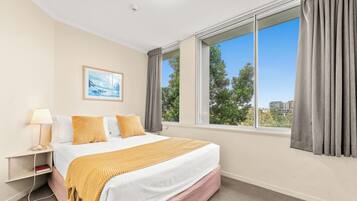 Una habitación de hotel con una cama, una mesita de noche, una lámpara, un cuadro y una ventana con cortinas.