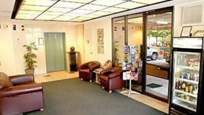 A lobby with leather sofas, a refrigerator, and a glass door leading outside. - Chasely Apartment Hotel (Auchenflower)