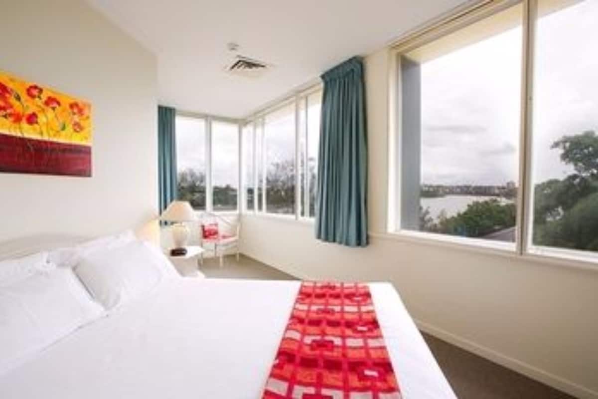 A hotel room with a large bed, a view of the city, and a painting on the wall.