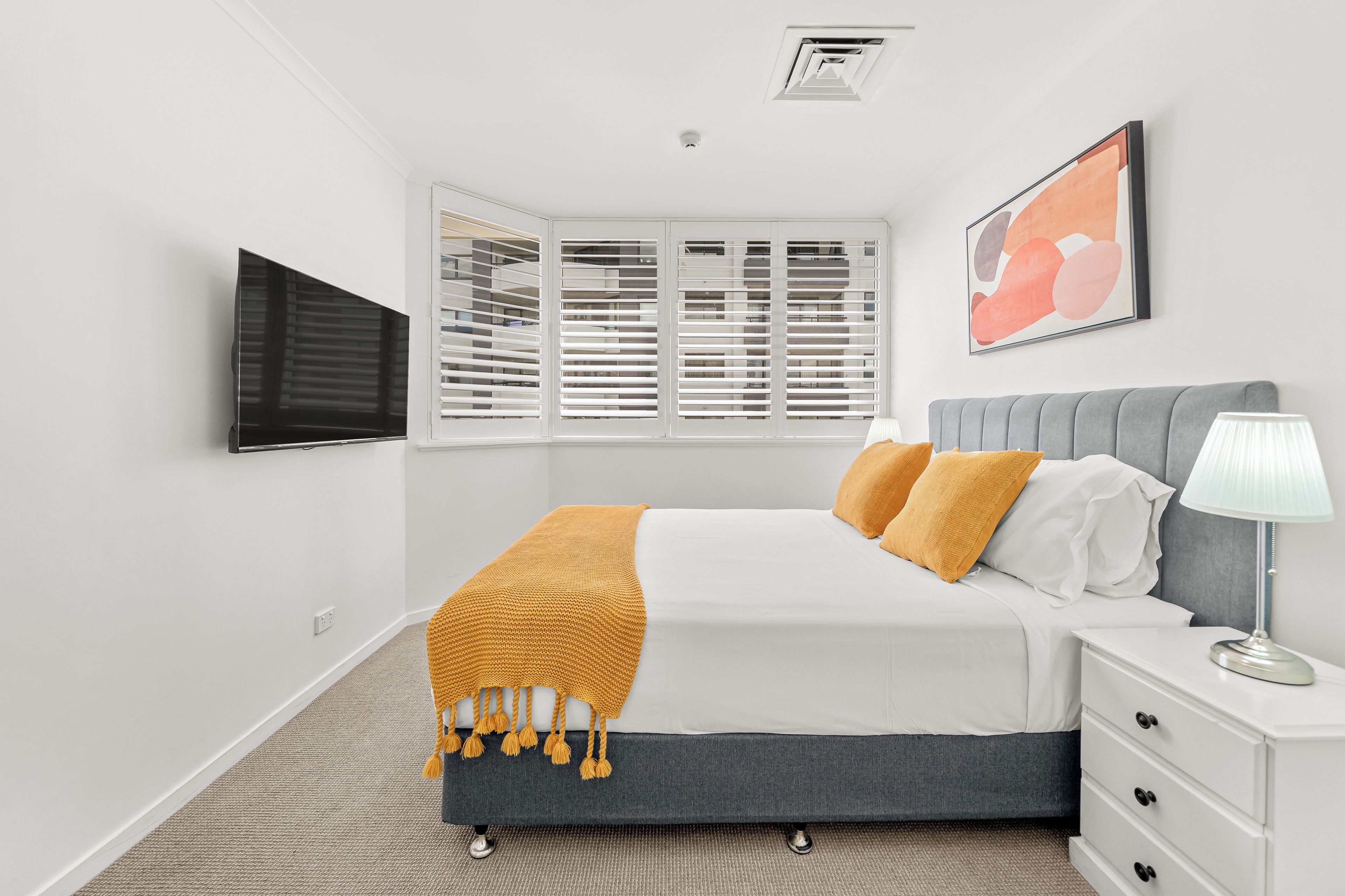 Un dormitorio con cama, mesita de noche, lámpara y ventana con persianas.