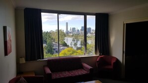 A room with a large window offering a view of a city skyline and a river. There is a red sofa and a chair in the room. - Chasely Apartment Hotel (Auchenflower)