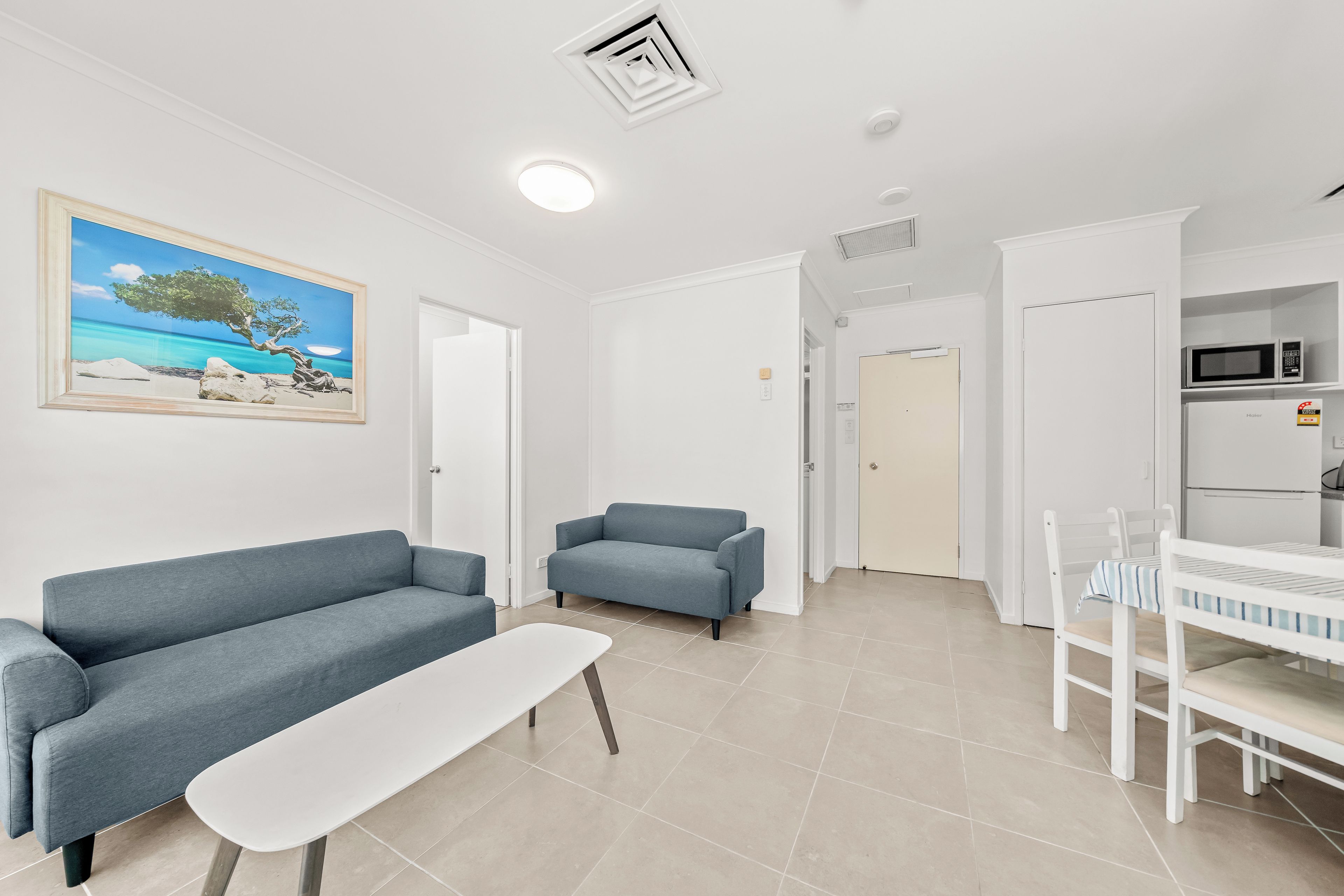 A modern living room with a blue sofa, a white table, and a painting of a beach scene.