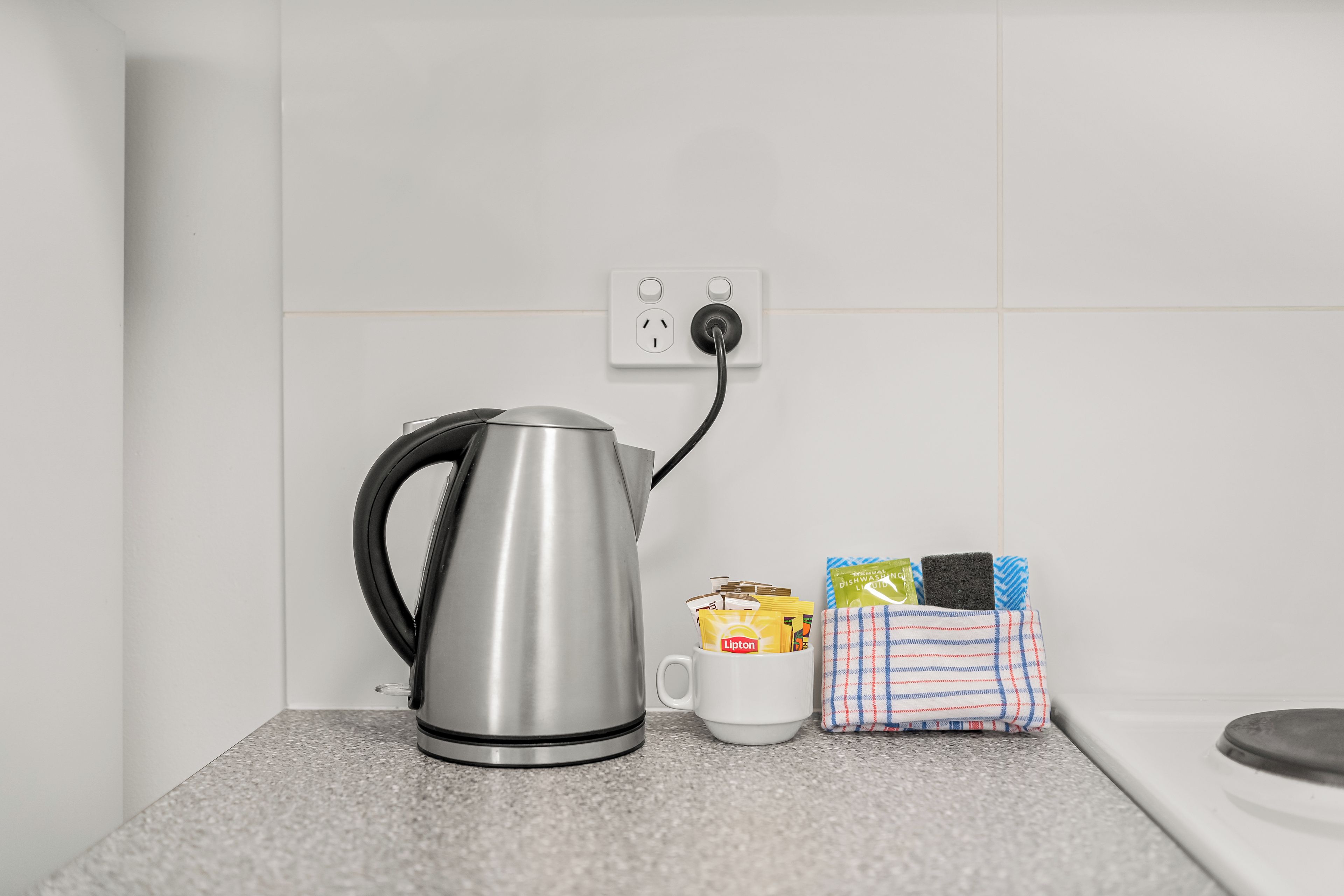 Une bouilloire posée sur un plan de travail, une tasse et un chiffon avec des produits de nettoyage.