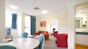 A hotel room with a dining area, a sofa, and a red chair. - Chasely Apartment Hotel (Auchenflower)
