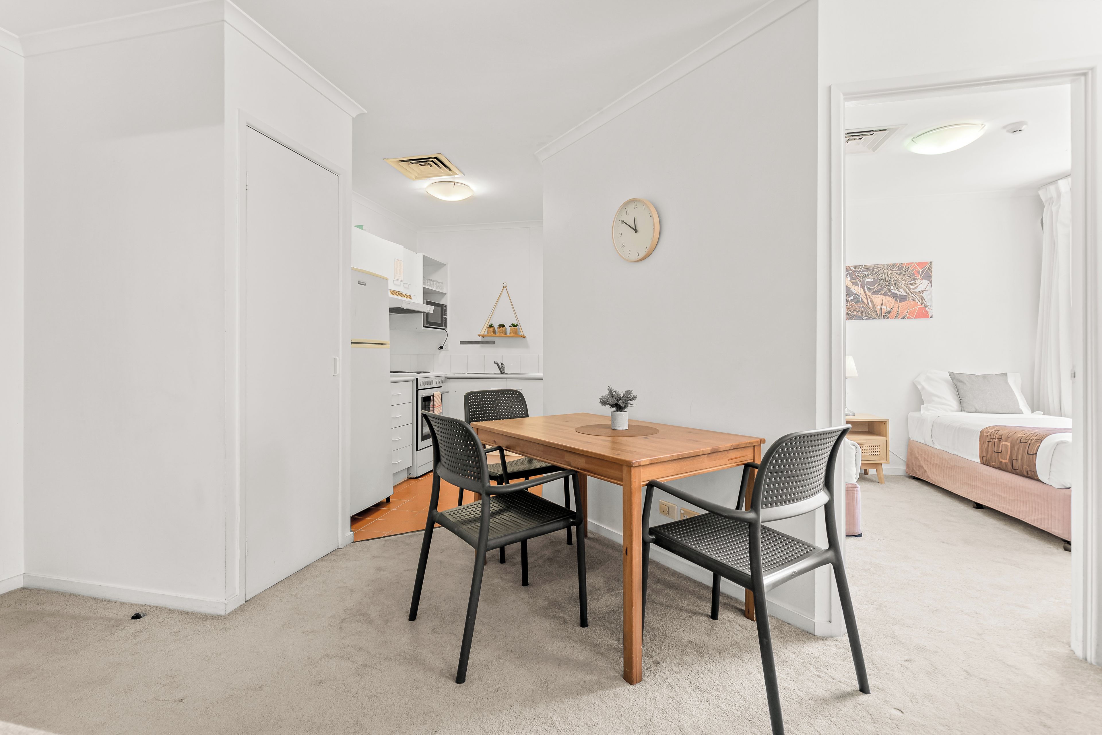 Une cuisine moderne avec des meubles blancs, une table à manger en bois et des chaises noires.