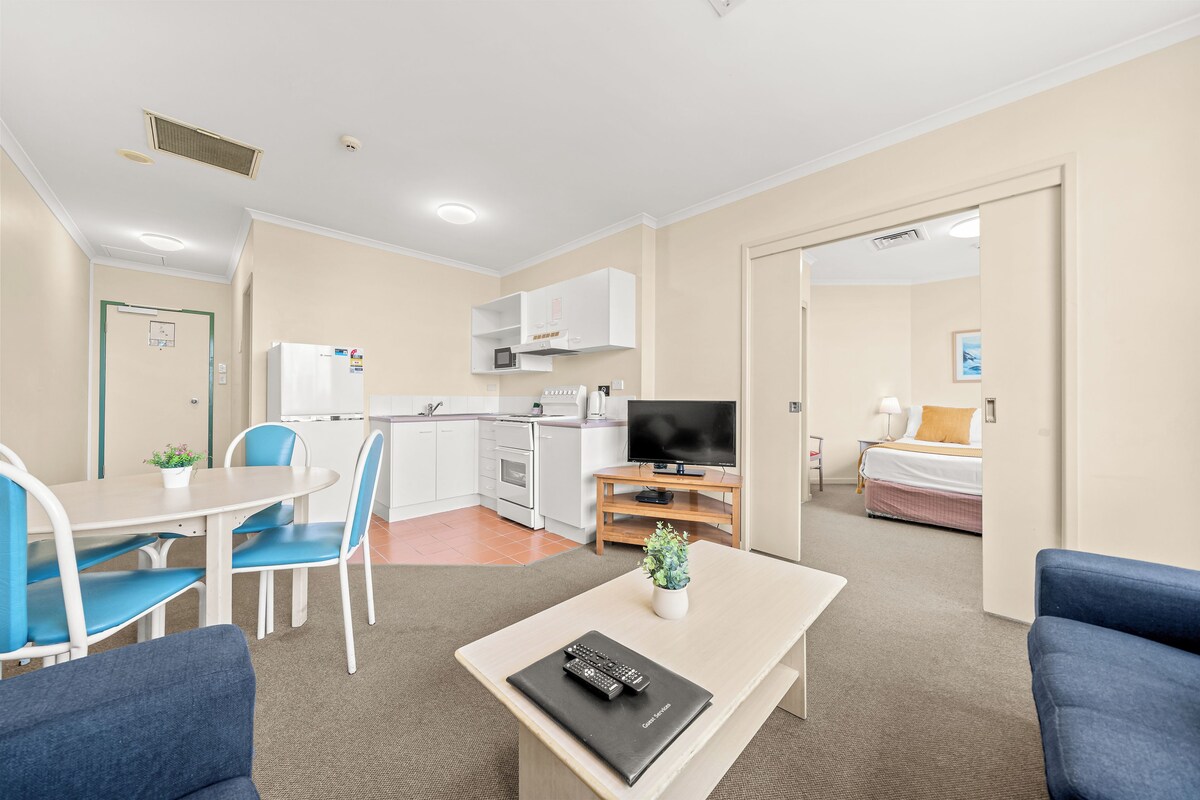A hotel room with a kitchenette, a dining area, a TV, and a bed.
