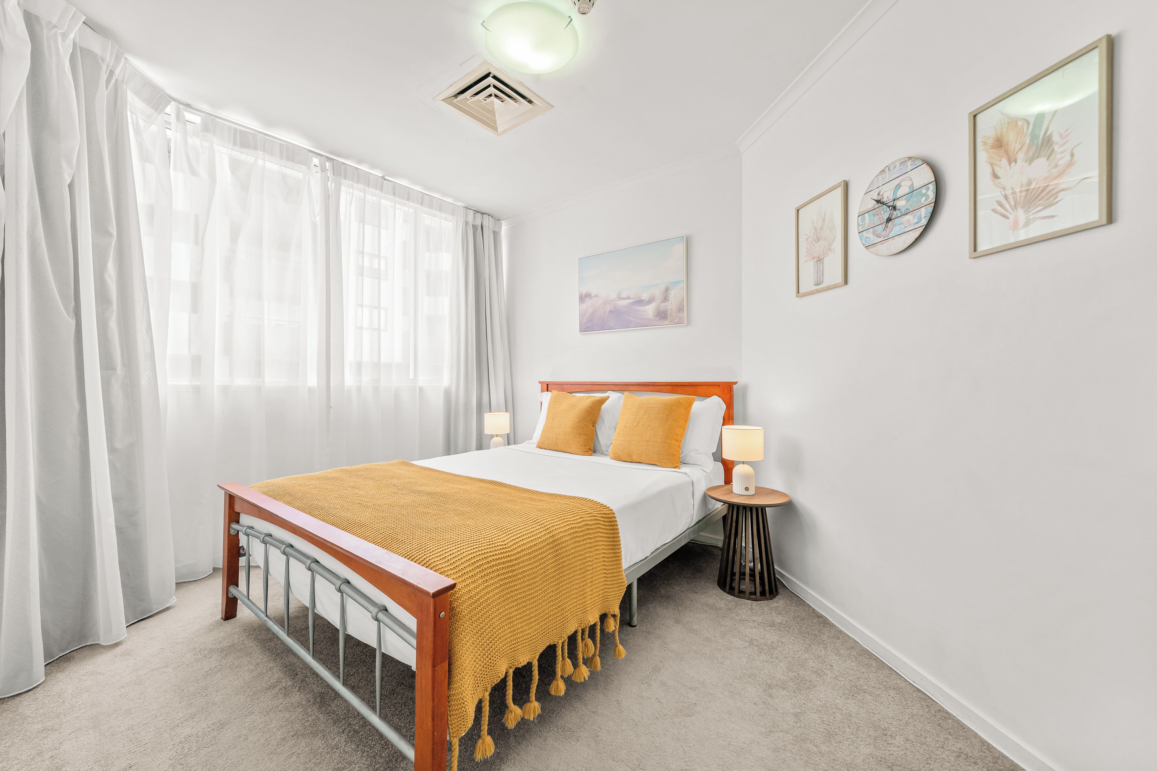 Une chambre à coucher avec un lit, une table de chevet, une lampe et une fenêtre avec des rideaux.