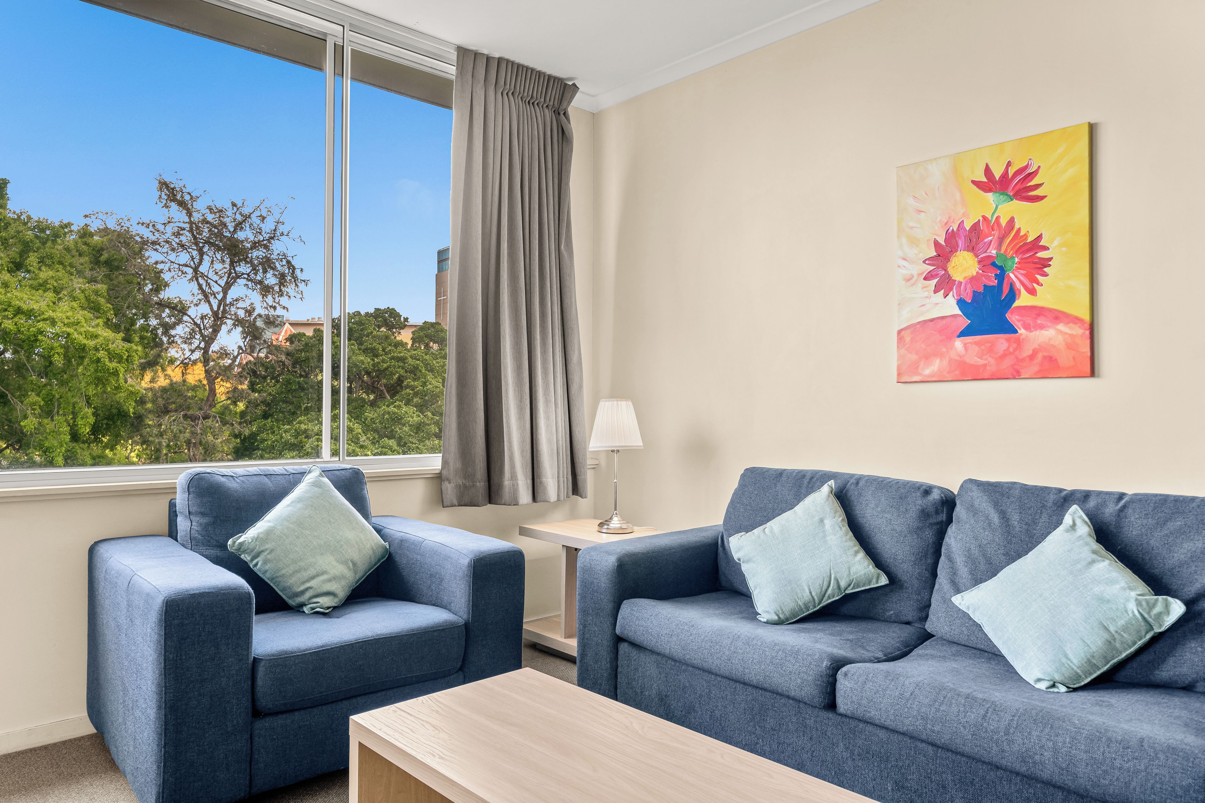 A room with a sofa set, a table, a lamp, a painting, and a window with curtains.