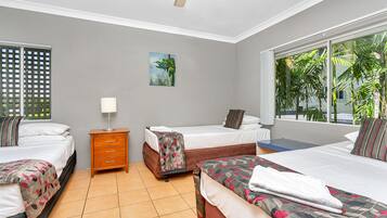 A hotel room with two beds, a nightstand, a painting, and a window with a view of palm trees.