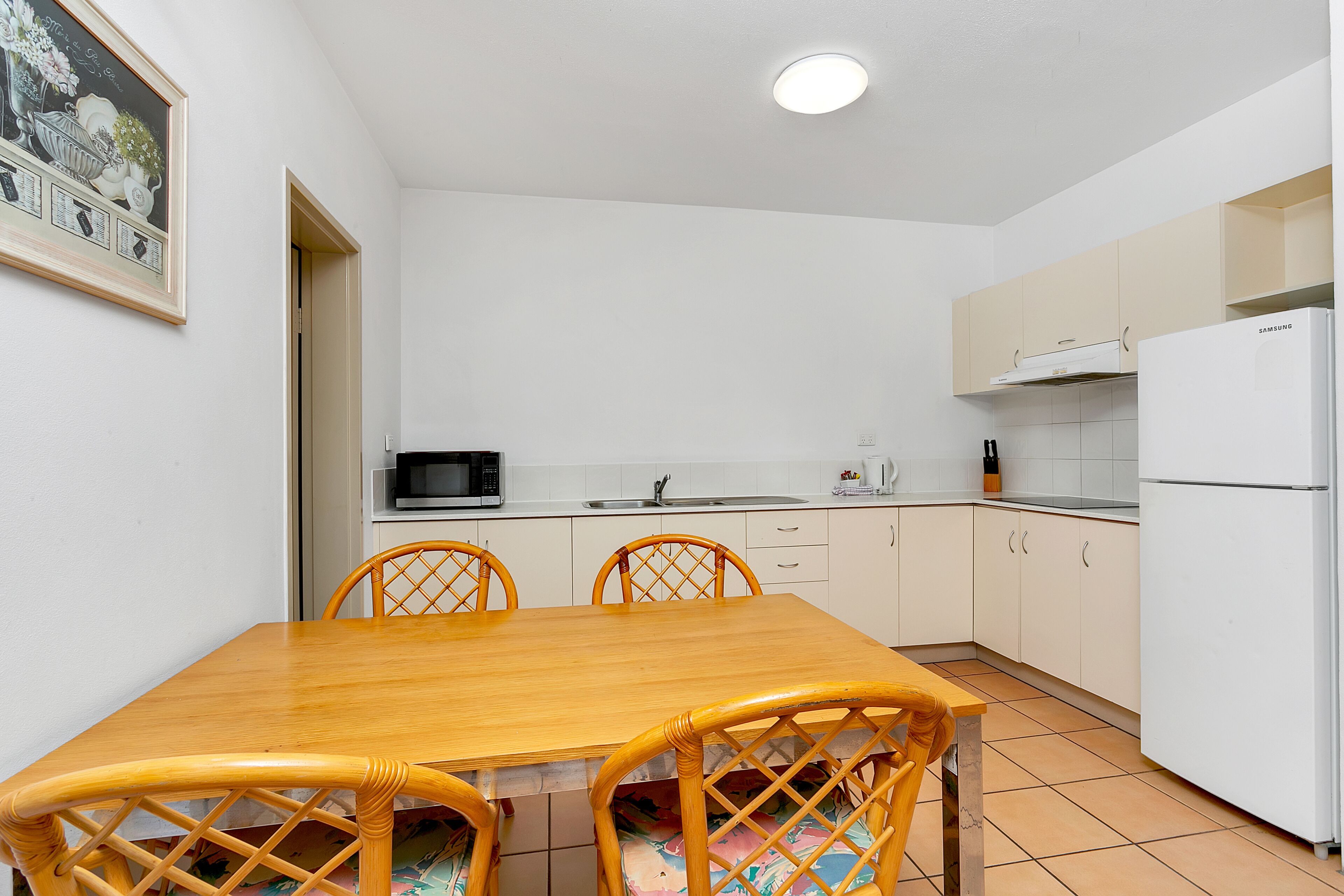 A compact kitchen with white cabinets, a wooden dining table, and a white refrigerator.