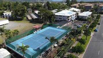 A large blue tennis court surrounded by a green fence, with a white building labeled "Motel" in the background.