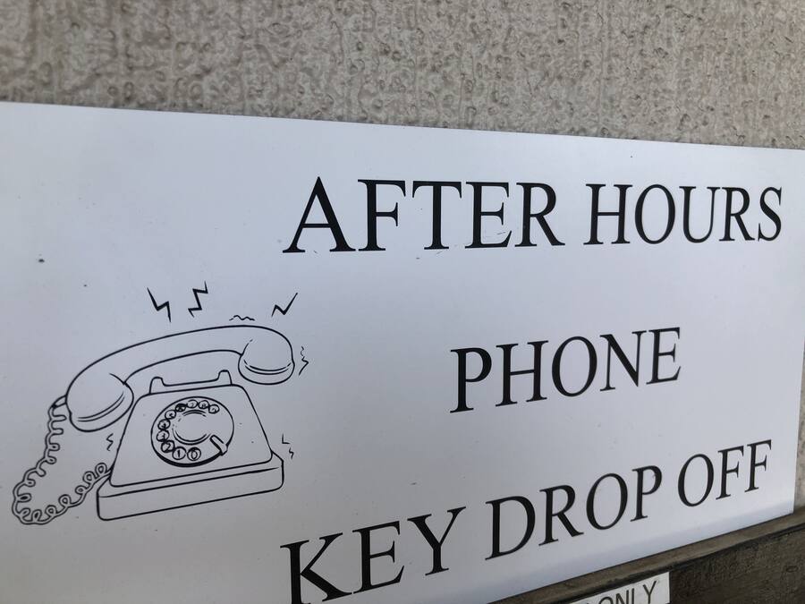 A sign with a telephone and the text "AFTER HOURS PHONE KEY DROP OFF".
