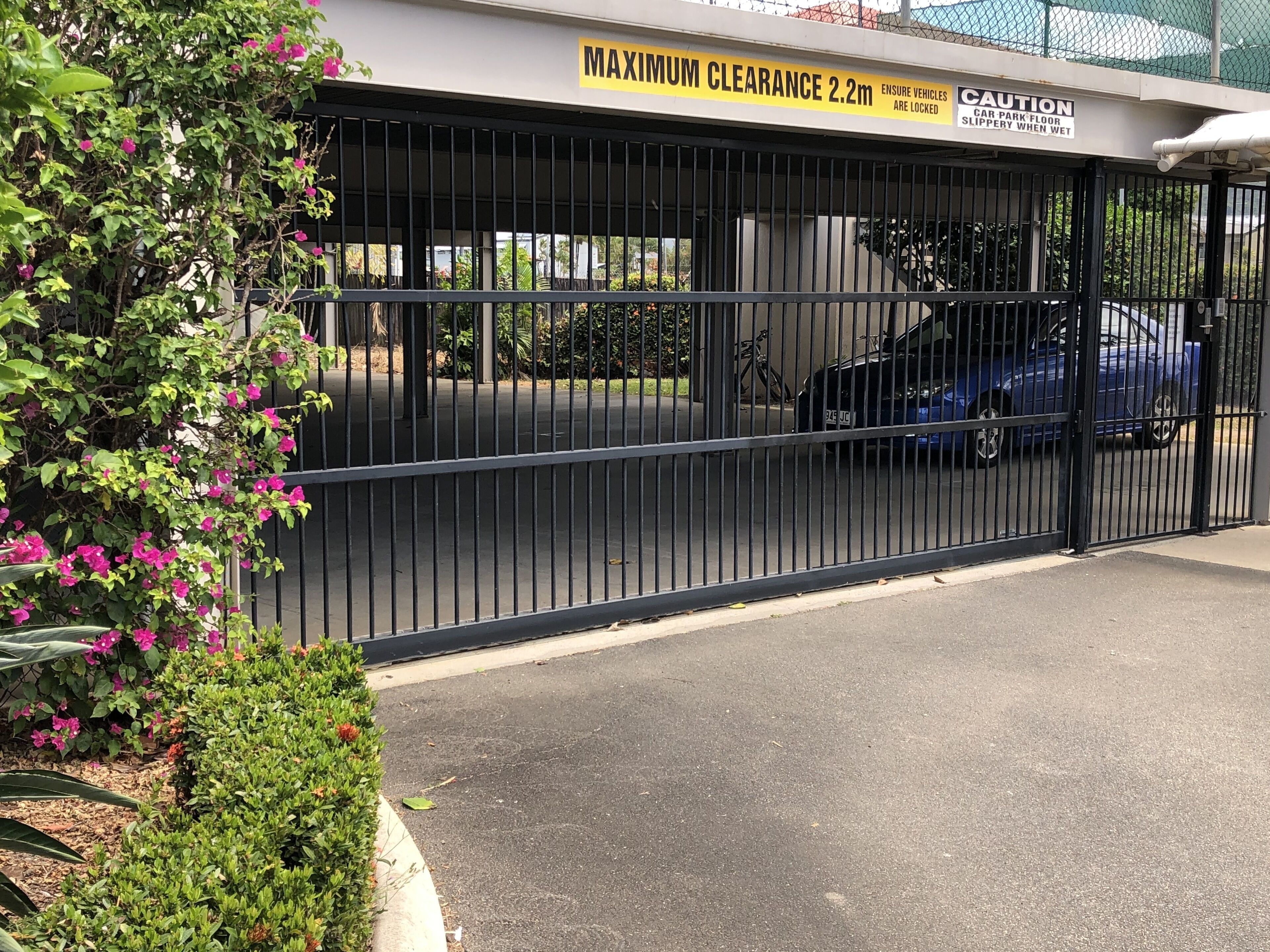 A gated parking area with a maximum clearance sign of 2.2m, a caution sign for slippery floors, and a locked car park.