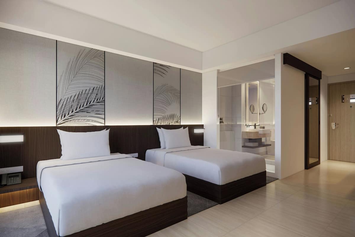 A modern hotel room with two beds, a large mirror, a built-in desk, and a separate bathroom.