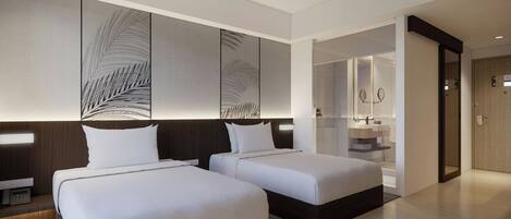 A modern hotel room with two beds, a large mirror, a built-in desk, and a separate bathroom.