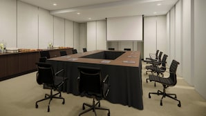 A conference room with a long table, chairs, a projector screen, and a podium.