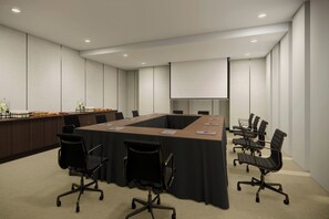 Une salle de conférence équipée d’une longue table, de chaises, d’un écran de projection et d’un pupitre.
