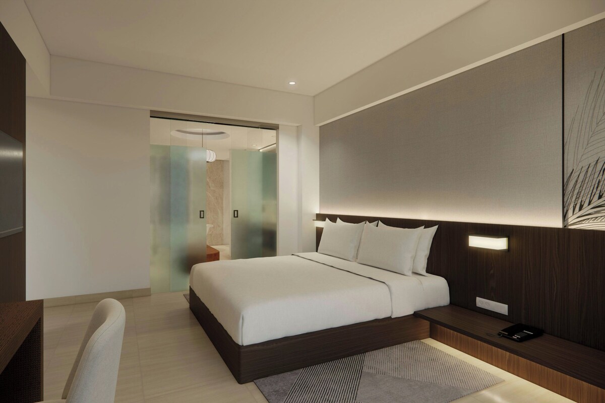 A modern hotel room with a large bed, a desk, and a nightstand.