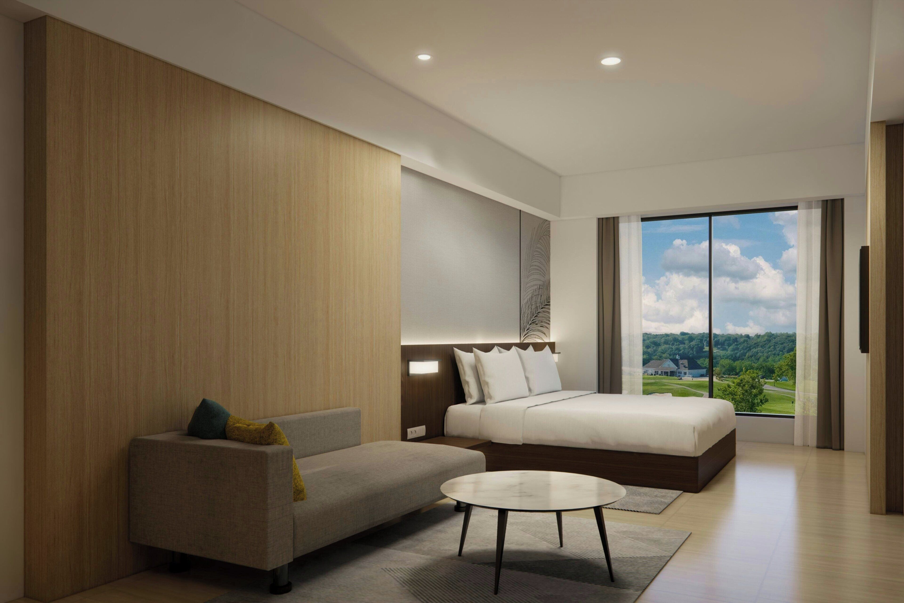 Habitación de hotel moderna con cama, sofá, una mesita y un ventanal que ofrece vistas al exterior.