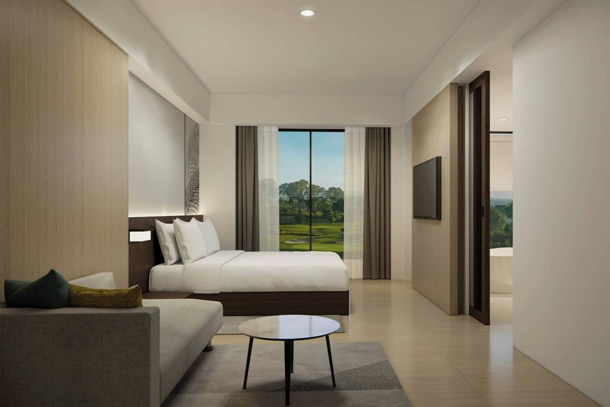 A modern hotel room with a bed, a sofa, a TV, and a view of a golf course.