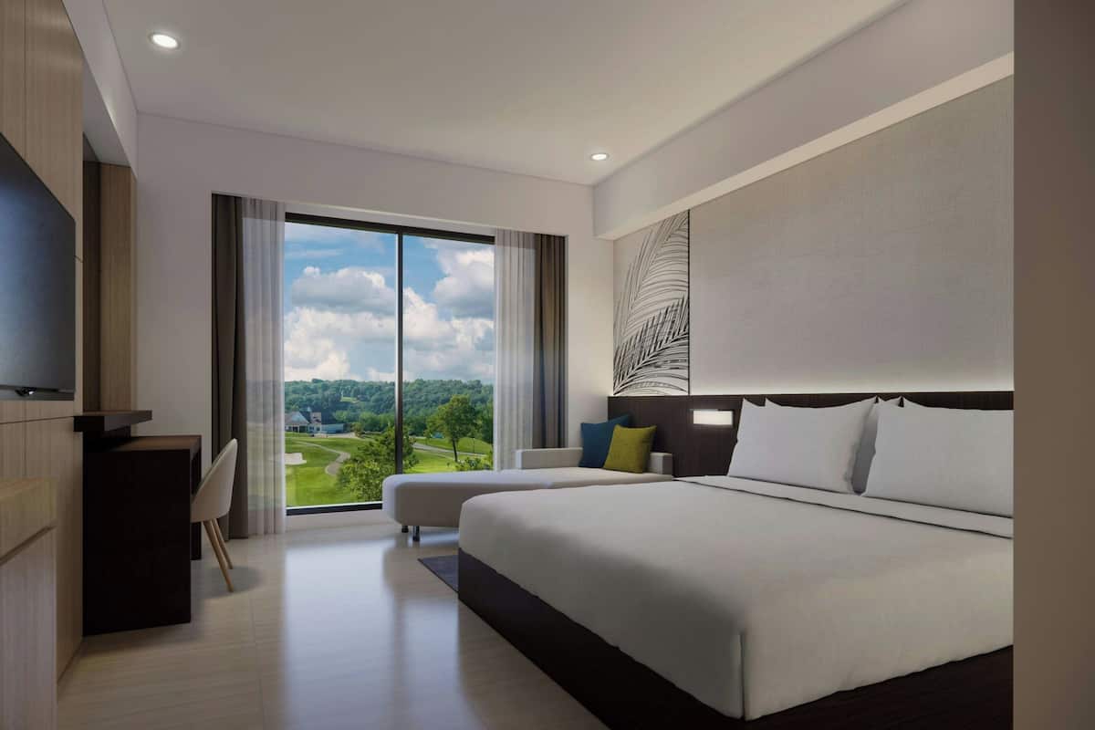 A modern hotel room with a large bed, a desk, and a view of a golf course.