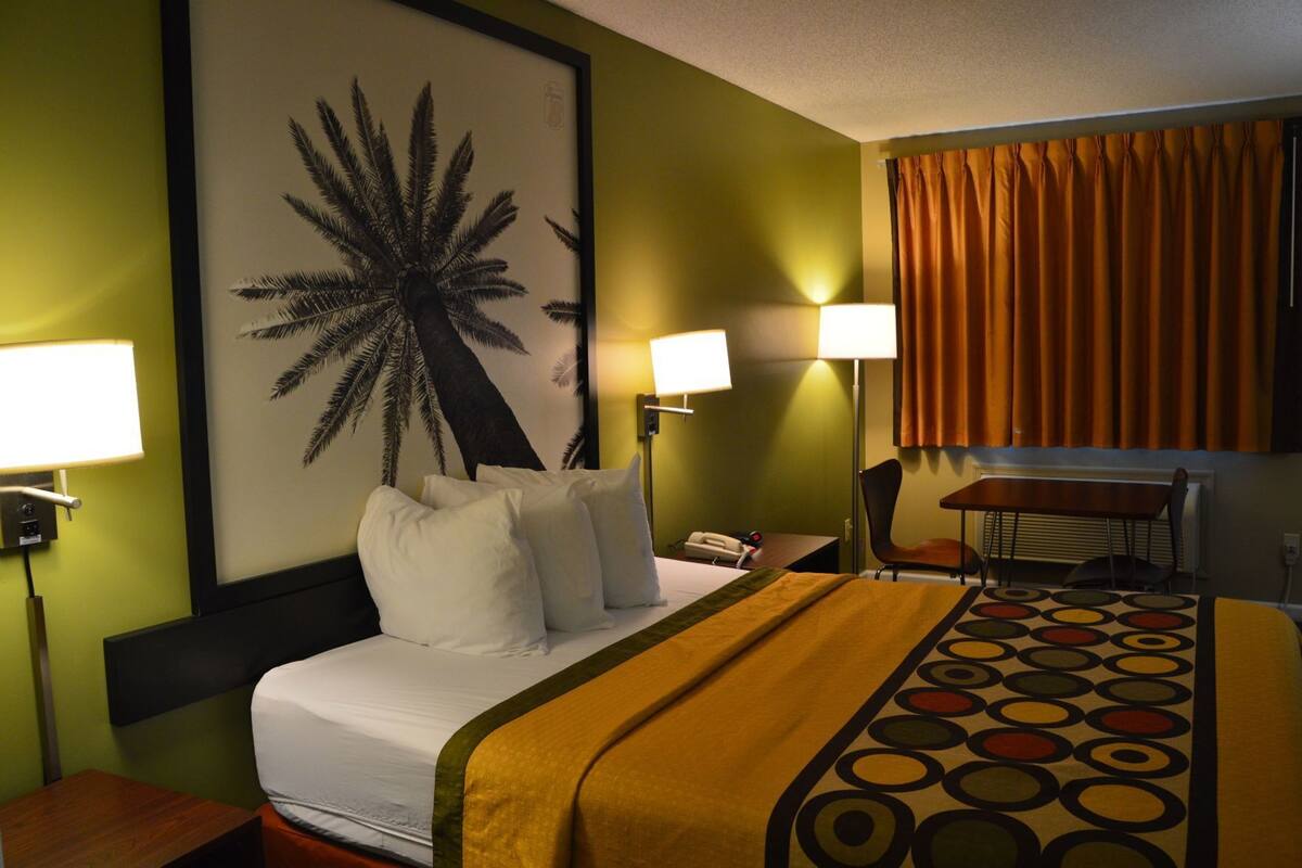 Une chambre d’hôtel comprenant un lit, deux lampes de chevet, un bureau, une chaise et un grand tableau mural.