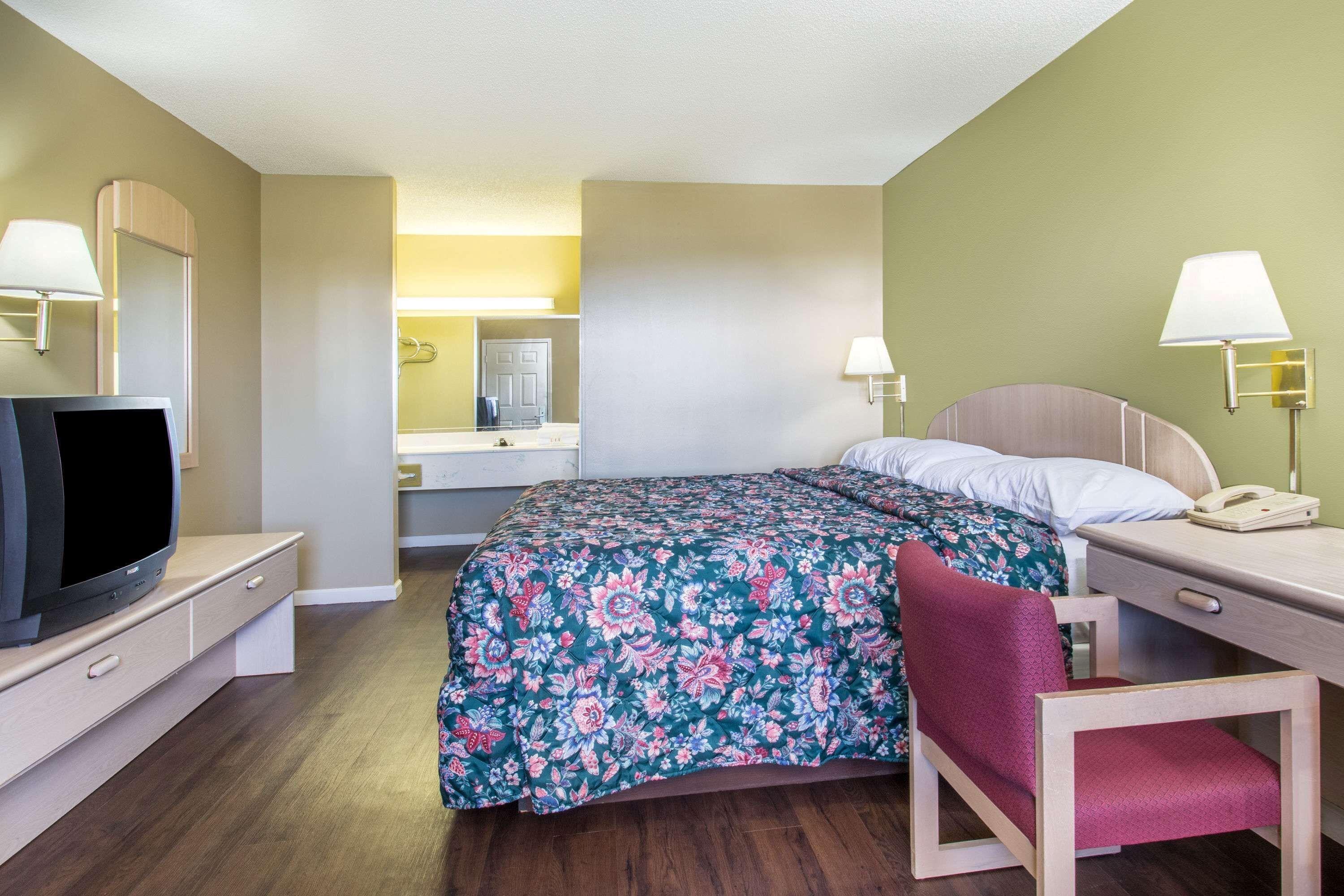 A hotel room with a bed, a desk, a chair, a television, and a phone.