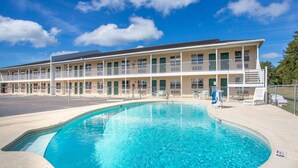 Un motel con piscina, zona de estacionamiento cercada y un edificio de dos pisos con balcones.