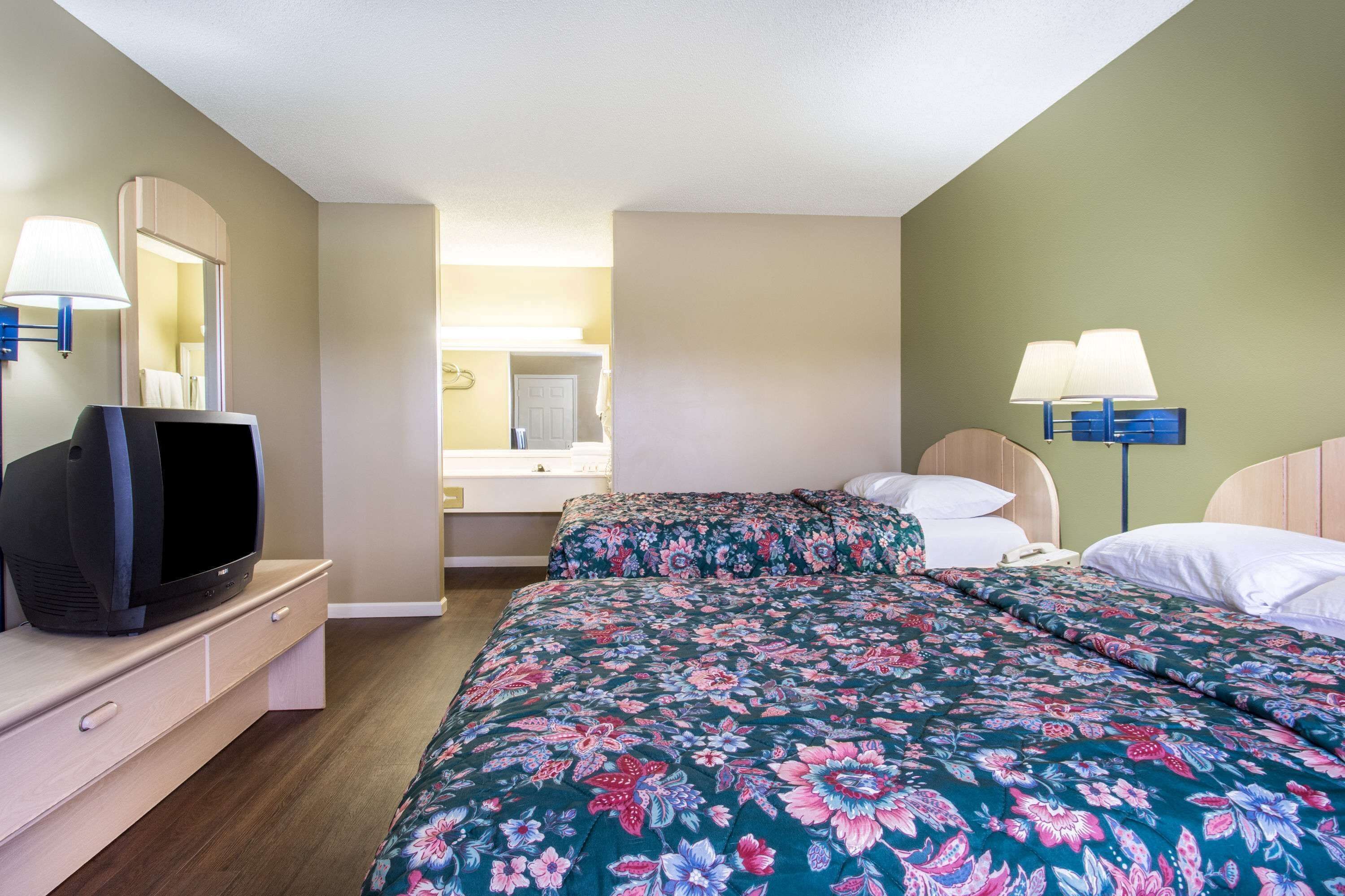 A hotel room with two beds, a TV on a dresser, and two wall-mounted lamps.