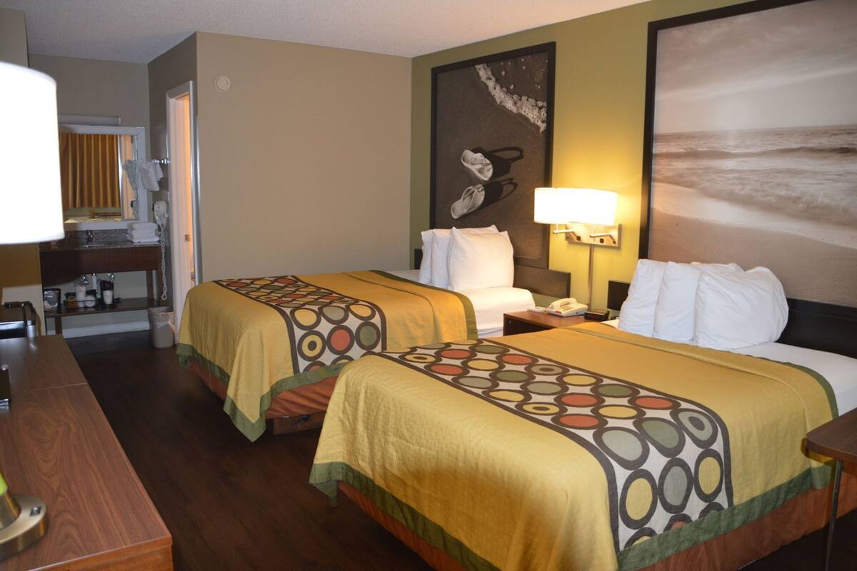 Une chambre d’hôtel avec deux lits, un bureau, une chaise, une lampe et un tableau au mur.