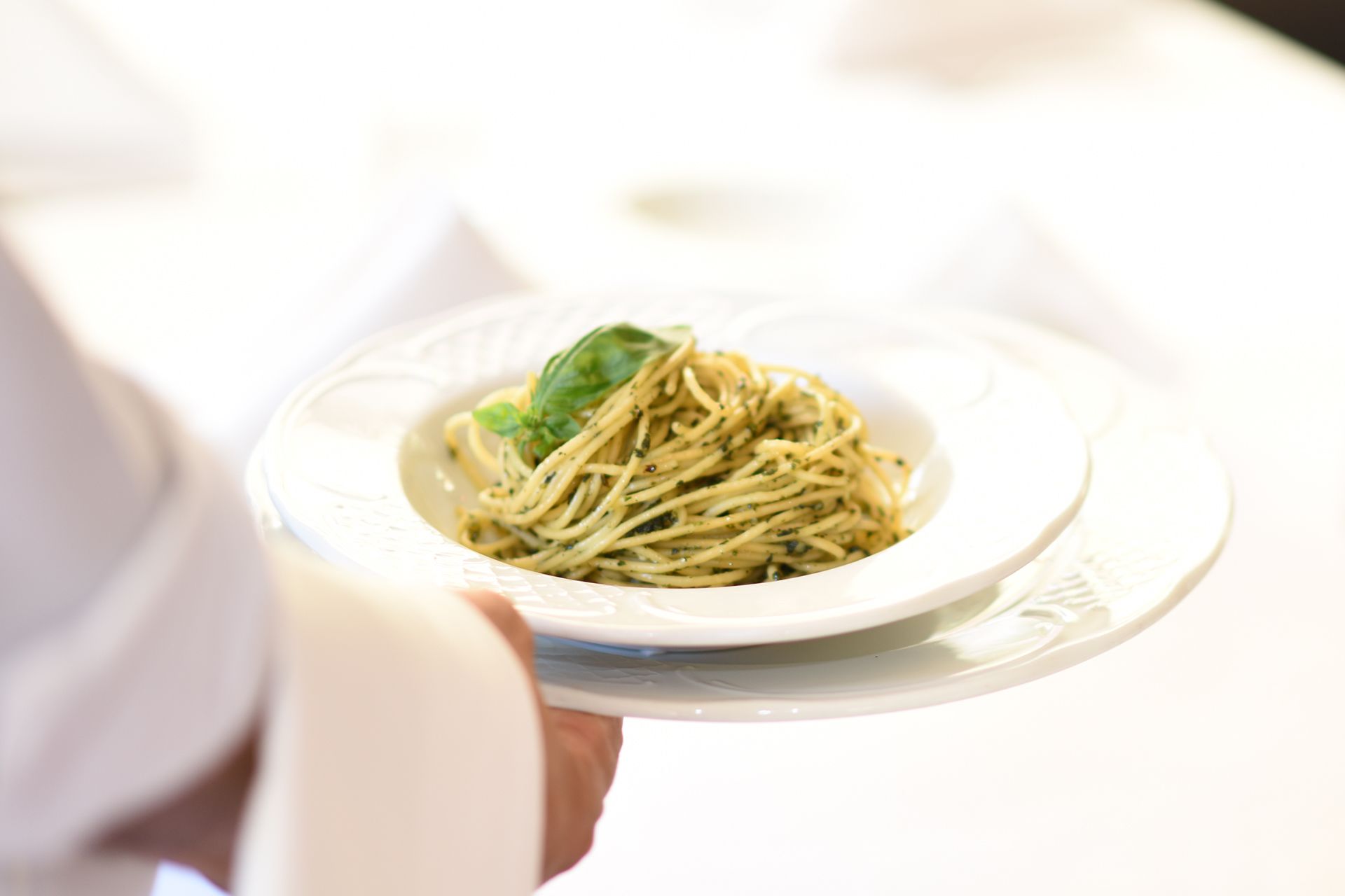 A plate of spaghetti with a garnish, held by a person.