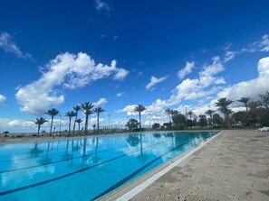A swimming pool with clear blue water, surrounded by palm trees and a clear sky. - Portemilio Hotel And Resort (Jounieh)