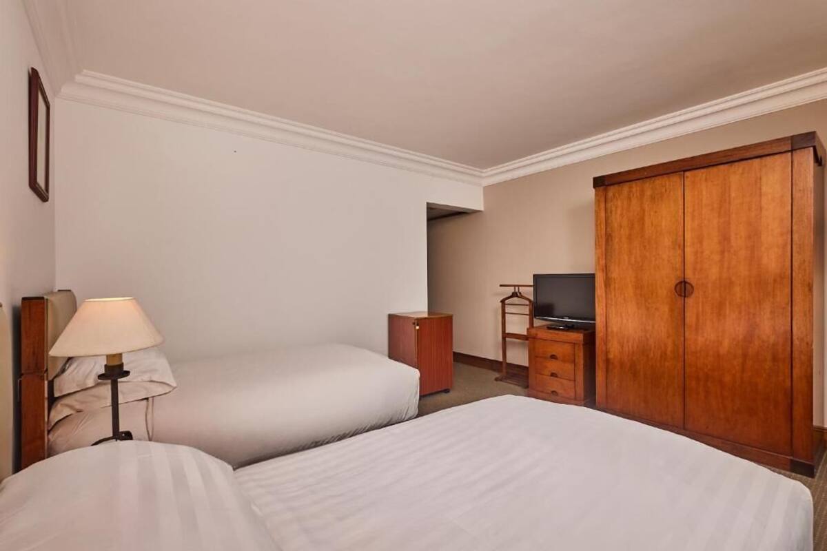 A hotel room with two beds, a TV, a wardrobe, and a lamp.