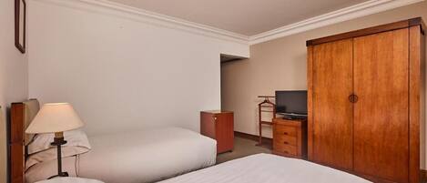 Habitación de hotel con dos camas, televisión, armario y lámpara.