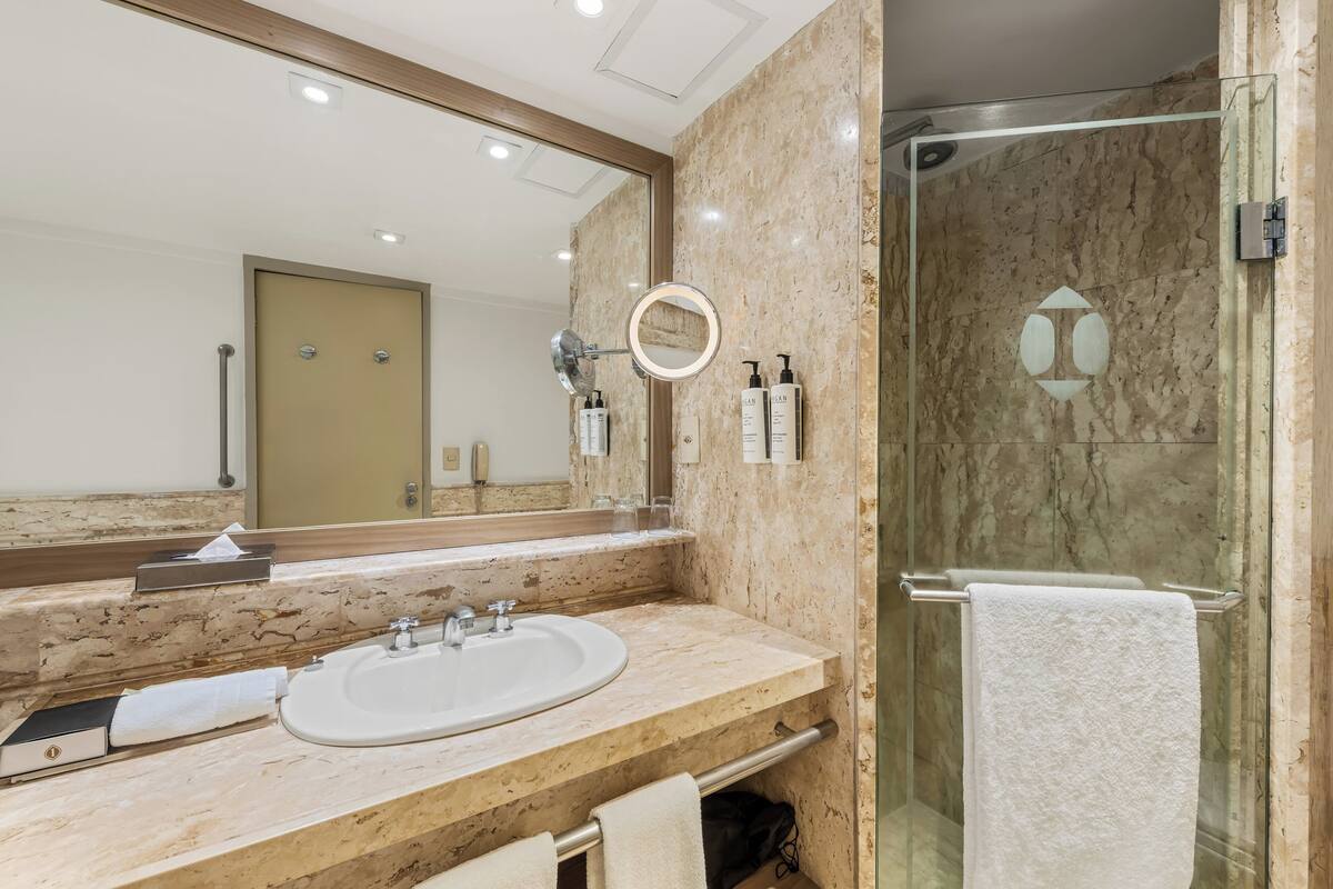Un baño con lavamanos de mármol, un espejo grande y una cabina de ducha de cristal.