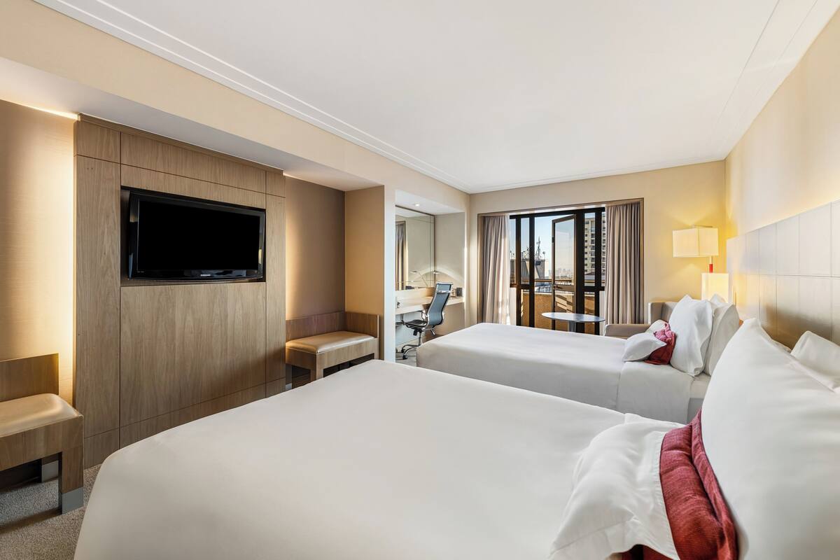 Habitación de hotel con dos camas, televisión, escritorio y vista a la ciudad.