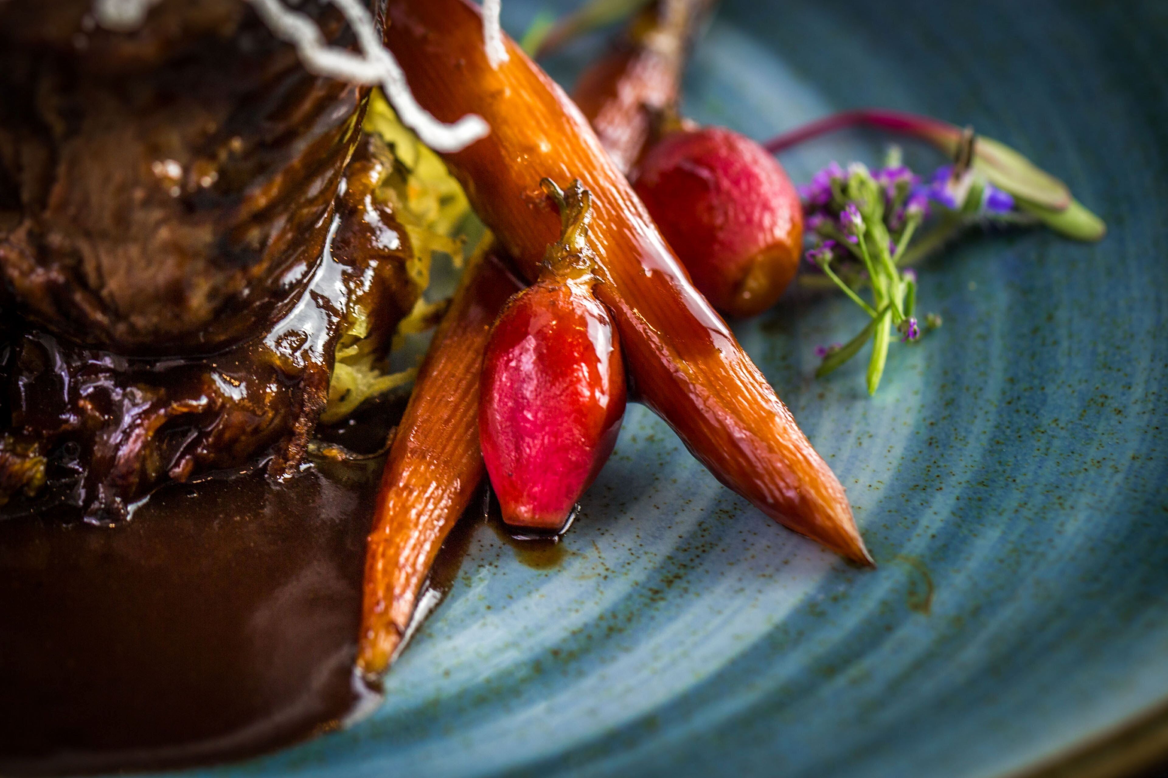 A close-up of a dish with glazed meat and carrots on a plate.