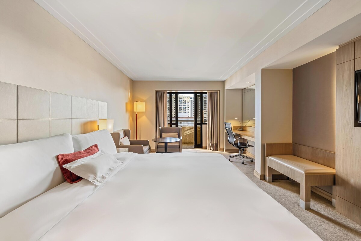 A hotel room with a large bed, a desk, a chair, and a bench.