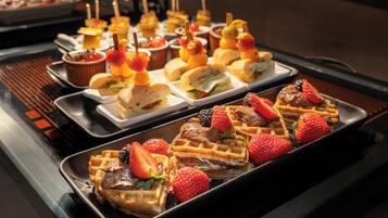 Un buffet con diversi tipi di cibo, tra cui waffle, panini e spiedini di frutta.