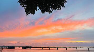 A sunset over a waterfront with a bridge and people walking.