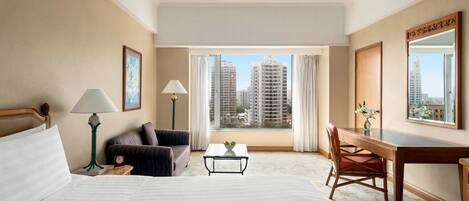 Habitación de hotel con una cama grande, un escritorio, una silla, una mesita y vistas a edificios altos.