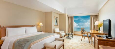 A hotel room with a large bed, a desk with a computer, a chair, and a view of the ocean.