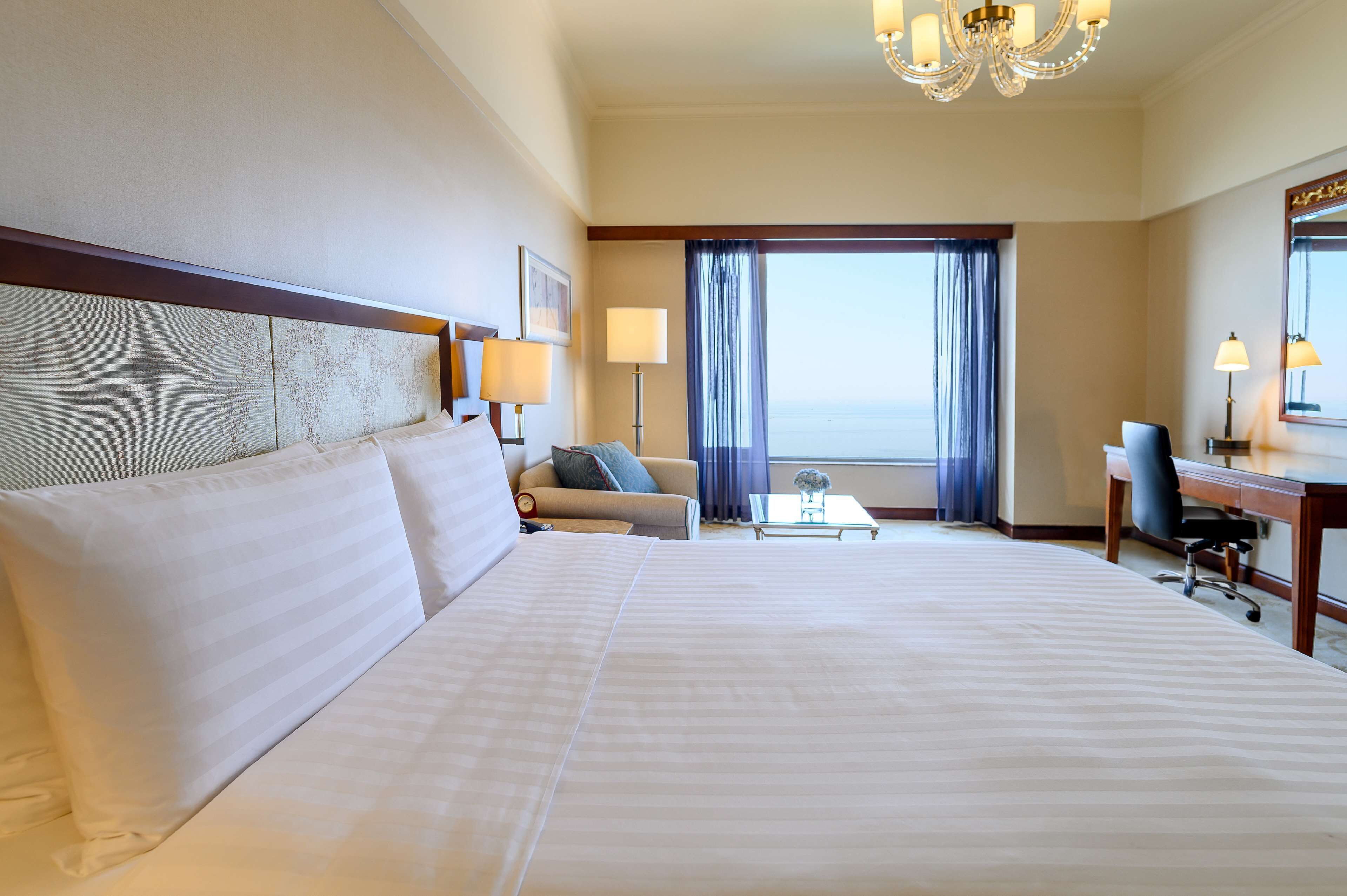 Une chambre d’hôtel avec un grand lit, un bureau, une chaise, un canapé et une vue sur l’océan.