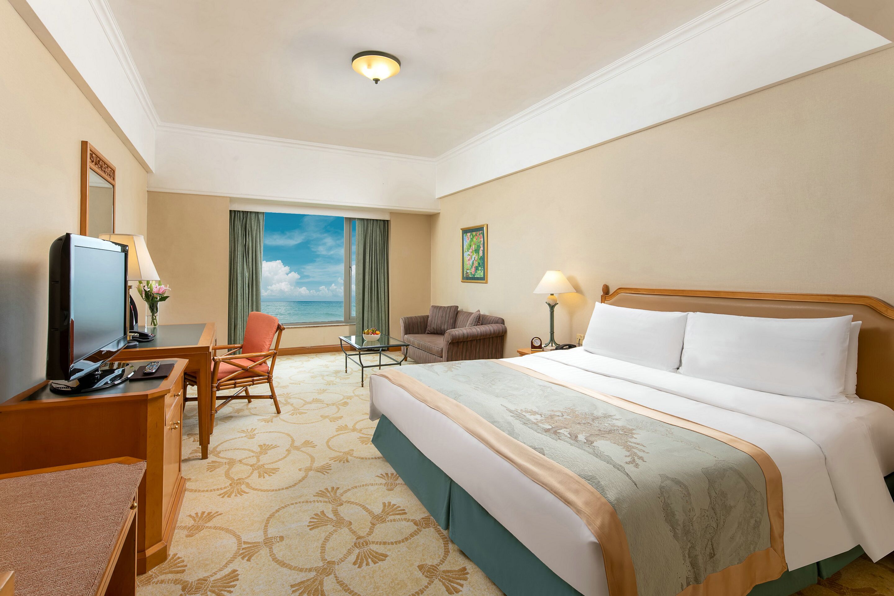 Une chambre d’hôtel avec un grand lit, un bureau avec un ordinateur, une chaise, une petite table avec une lampe et une vue sur le ciel par une fenêtre.