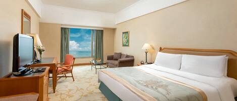 Une chambre d’hôtel avec un grand lit, un bureau avec un ordinateur, une chaise, une petite table avec une lampe et une vue sur le ciel par une fenêtre.